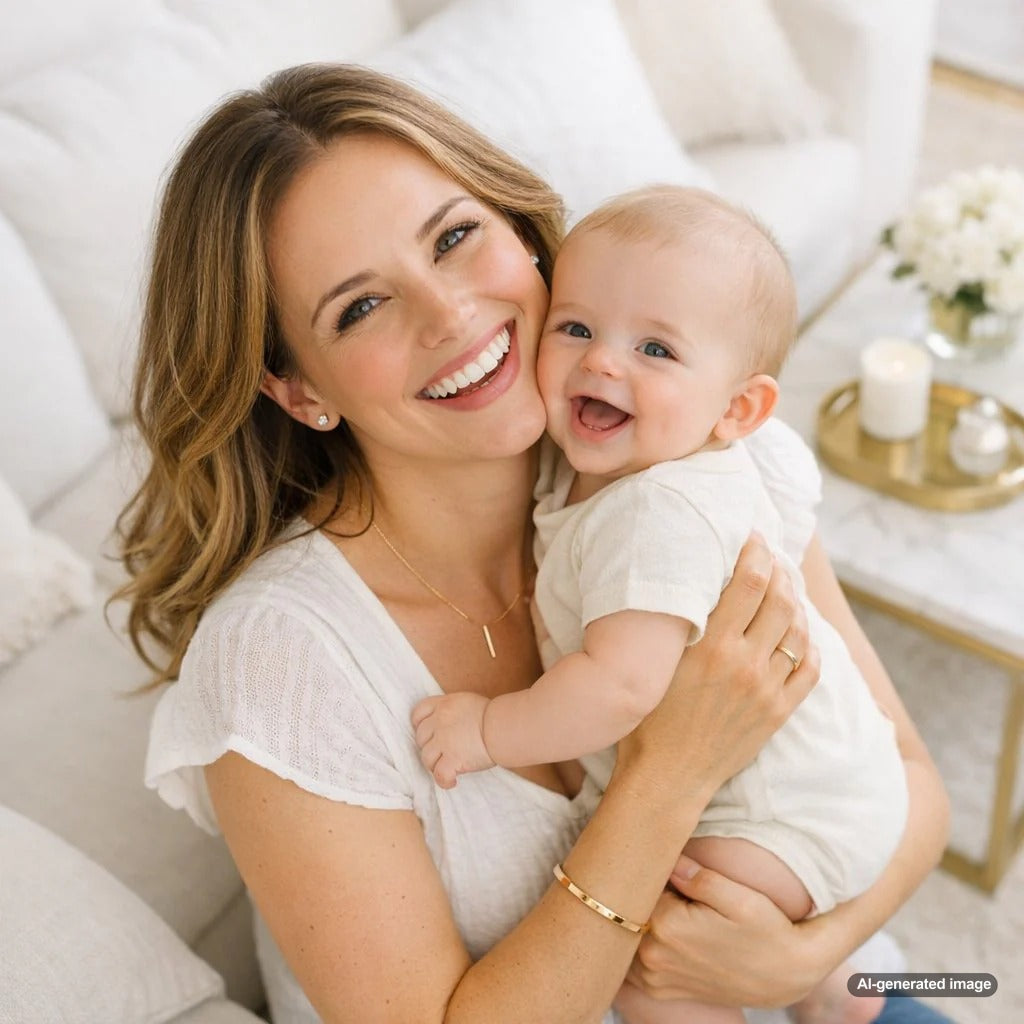 A new mother smiling while gently cuddling her baby, wearing simple and beautiful diamond stud earrings and a delicate pendant necklace that are both stylish and baby-safe.