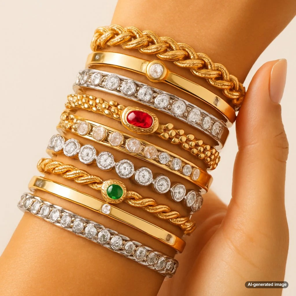 An artfully stacked wrist showcasing a mix of gold, silver, and rose gold bracelets with various textures including chains, cuffs, and gemstone accents.