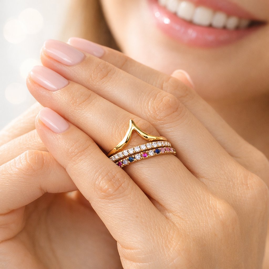 A beautifully styled flat lay of multiple wishbone or chevron rings stacked together in gold and rose gold, alongside other delicate band rings, on a neutral background.