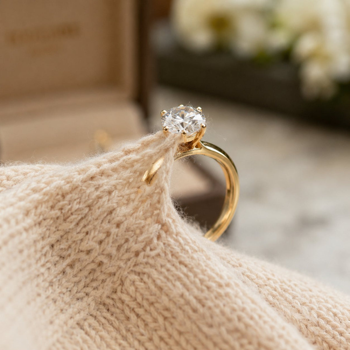 Close up of a womans hand wearing a diamond engagement ring next to a cozy red sweater to demonstrate fabric snagging